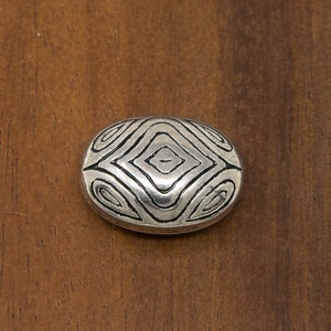 May include: A silver oval-shaped bead with a geometric pattern.