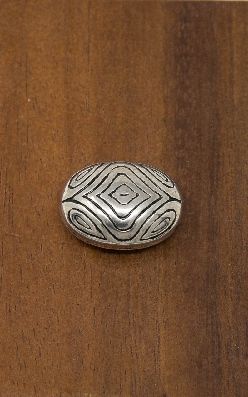 May include: A silver oval-shaped bead with a geometric pattern.