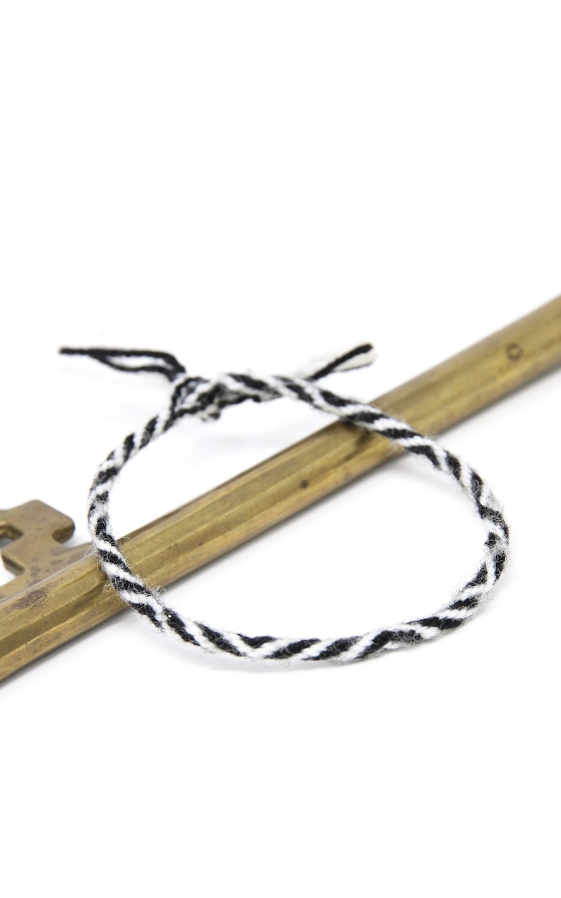 May include: A black and white braided cord wrapped around a brass key.