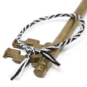 May include: A brass key with a black and white braided cord tied around it. The cord is tied in a knot at the top of the key and has two loose ends.