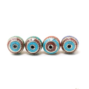 May include: Four round beads with intricate designs. Each bead is a different color: turquoise, green, red, and blue. The beads are made of metal and have a silver finish.
