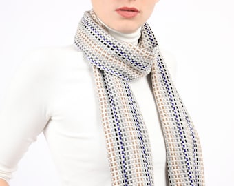 May include: A woman wearing a white turtleneck sweater with a brown, white, and purple patterned scarf.