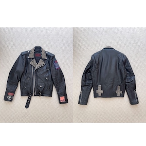 Può includere: Giubbotto in pelle nera da motociclista con borchie e toppe argentate. La giacca ha una chiusura con cerniera, una cintura e un colletto con borchie.