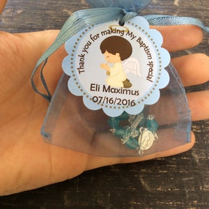 May include: Blue organza bag with a white and brown tag that says "Thank you for making my Baptism special Eli Maximus 07/16/2016". The tag has a cartoon image of a boy angel with brown hair and a halo. A blue and silver rosary is inside the bag.