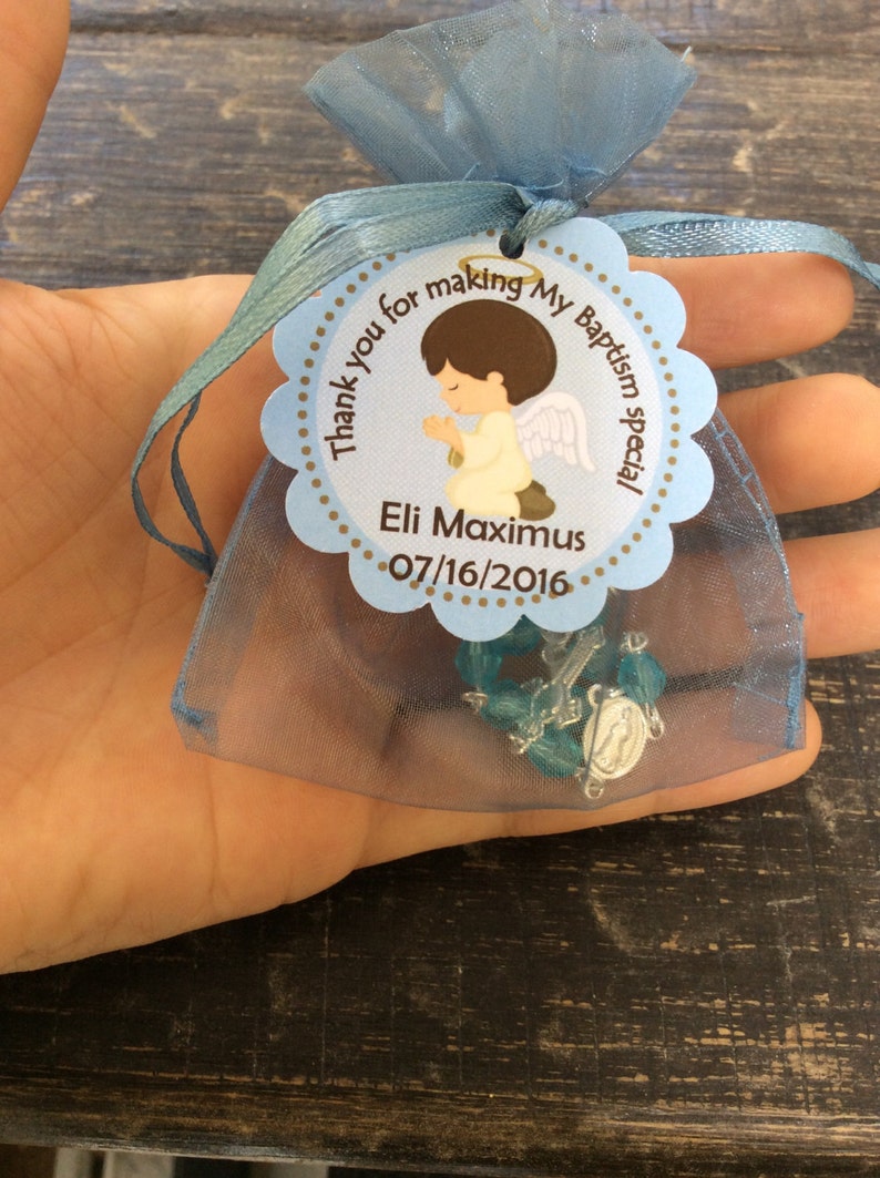 May include: Blue organza bag with a white and brown tag that says "Thank you for making my Baptism special Eli Maximus 07/16/2016". The tag has a cartoon image of a boy angel with brown hair and a halo. A blue and silver rosary is inside the bag.