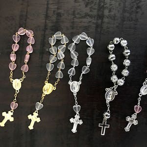 May include: Four heart-shaped bead rosaries with gold and silver accents. Two rosaries have pink beads, one has clear beads, and one has silver beads.