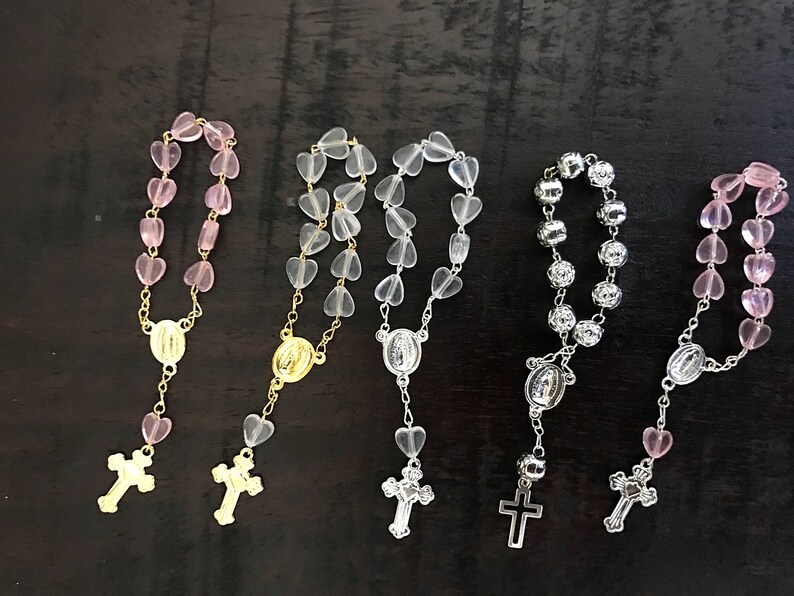 May include: Four heart-shaped bead rosaries with gold and silver accents. Two rosaries have pink beads, one has clear beads, and one has silver beads.