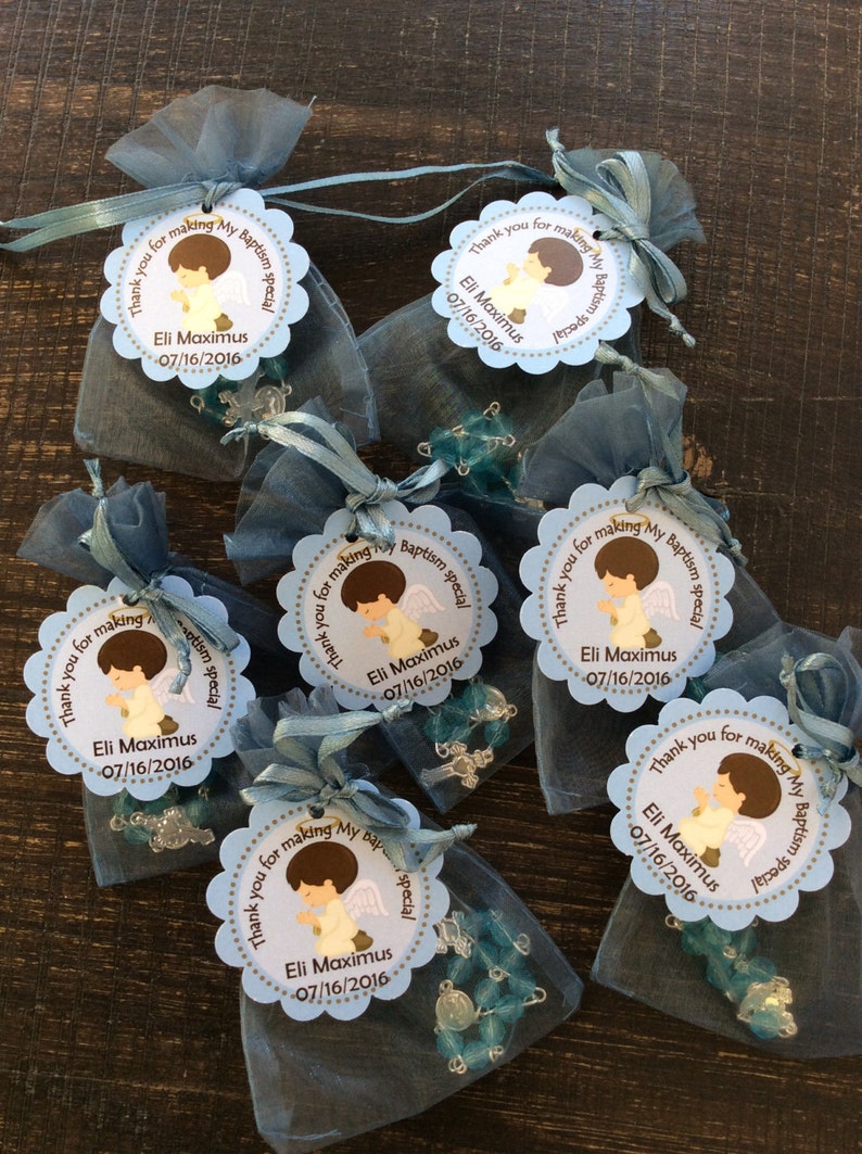 May include: Blue organza bags filled with blue and silver rosary beads and tied with a blue ribbon. Each bag has a round, scalloped, light blue tag with a brown illustration of a boy angel with the text "Thank you for making my baptism special" and "Eli Maximus 07/16/2016".