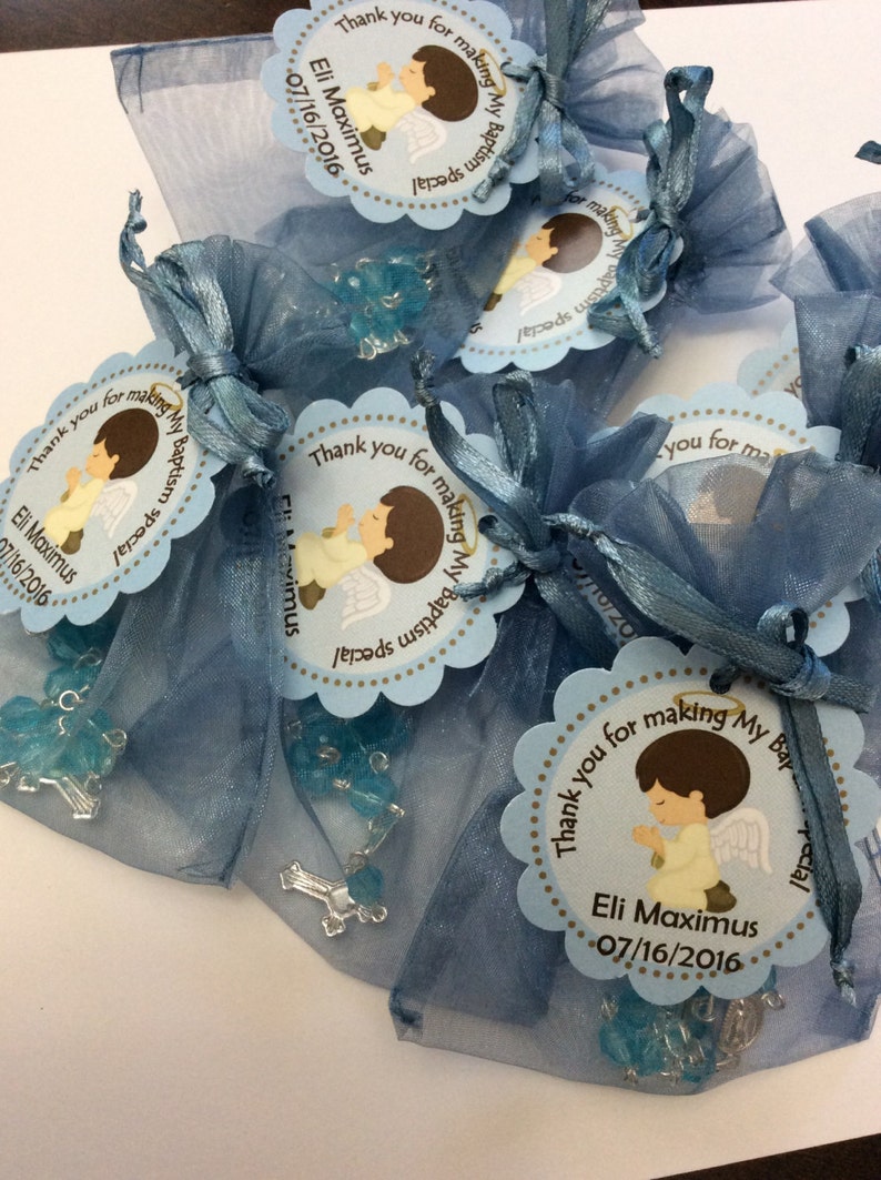 May include: Blue organza bags filled with blue and silver rosary beads and a thank you tag with a cartoon angel and the text "Thank you for making my baptism special Eli Maximus 07/16/2016".