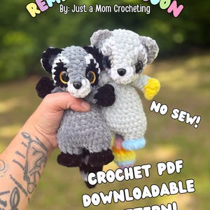 May include: Two crocheted raccoon plushies, one in gray and black, the other in light gray. The text "REMI THE RACCOON" and "CROCHET PDF DOWNLOADABLE PATTERN!" are displayed. The plushies are handmade and have yellow, black, and rainbow accents.