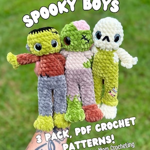 May include: Three plush crochet dolls featuring a Frankenstein-style monster, a zombie, and a skeleton. The text SPOOKY BOYS 3 PACK, PDF CROCHET PATTERNS! By: Just a Mom Crocheting is displayed over the dolls made of soft, textured yarn.