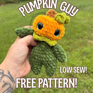 May include: A crocheted pumpkin figure with a bright orange head, a small brown stem, and a curly green leaf. The body is dark green with textured yarn. It features large, glossy blue eyes and text that reads BY JUST A MOM CROCHETING PUMPKIN GUY LOW SEW! FREE PATTERN! SAVE ME FOR LATER!