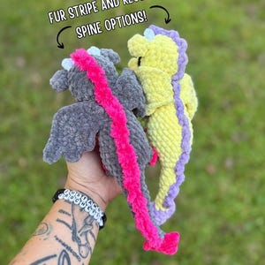 May include: Two handmade crochet dragon plushies. One is gray with a pink fur spine, the other is yellow with a purple spine. The text above reads "FUR STRIPE AND REGULAR SPINE OPTIONS!"