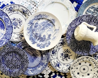 May include: A collection of blue and white ceramic plates with floral and landscape designs. The plates are arranged in a circular pattern on a crocheted surface. A white ceramic pitcher is in the center of the arrangement.