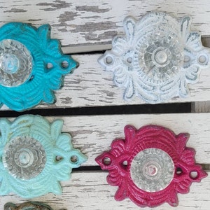 May include: Four decorative doorbells with ornate metal frames and clear glass centers. The doorbells are painted in turquoise, white, light blue, and pink.