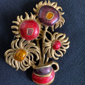 May include: A gold-toned brooch featuring a bouquet of stylized sunflowers in a vase. The flowers are enameled in shades of red, orange, and purple, with gold accents.