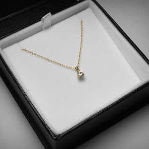 May include: A gold necklace with a single, round diamond pendant, presented in a black jewelry box with a white interior. The necklace chain is delicate, and the diamond sparkles.