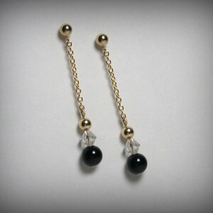 May include: A pair of gold dangle earrings with black beads and clear crystal accents.