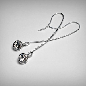 May include: A pair of silver earrings with clear crystal stones. The earrings are dangle style with a simple design.