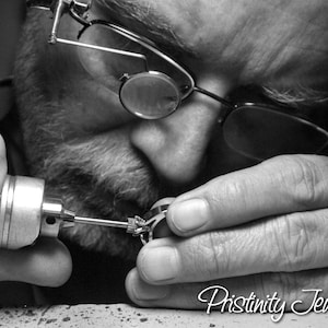 May include: Black and white image of a jeweler working on a ring. The jeweler is wearing glasses and using a small tool to refine the ring's details. The text "Pristinity Jewelry" is visible at the bottom of the image.