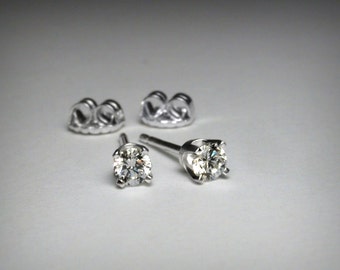 May include: A pair of silver stud earrings with a round, clear diamond in each earring.