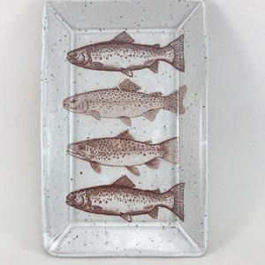 May include: A white ceramic rectangular serving tray with a speckled glaze and a brown outline. Four brown trout are printed on the tray.