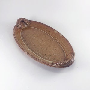 May include: A brown oval ceramic serving tray with a textured surface and two sculpted handles.