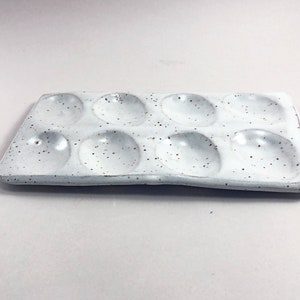 Puede incluir: Paleta de pintura de cer&aacute;mica blanca con nueve pozos redondos. La paleta tiene un esmalte moteado.