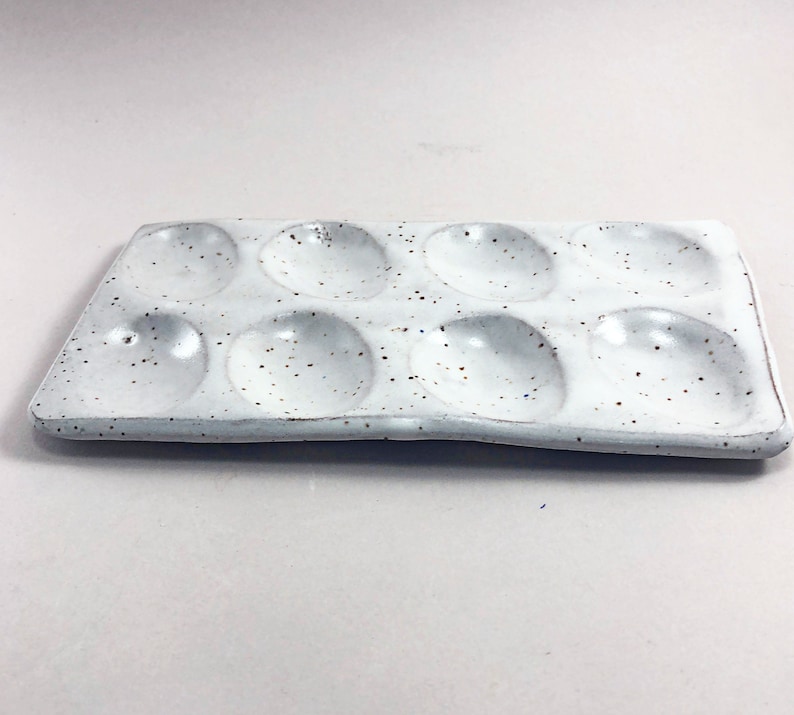 Puede incluir: Paleta de pintura de cer&aacute;mica blanca con nueve pozos redondos. La paleta tiene un esmalte moteado.