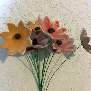 May include: A bouquet of ceramic flowers with orange and pink petals and black centers. The flowers are arranged on green stems.