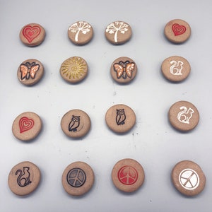 May include: A set of 15 round ceramic tiles with various designs, including hearts, butterflies, owls, cats, and peace signs. The tiles are all beige with brown and white accents.