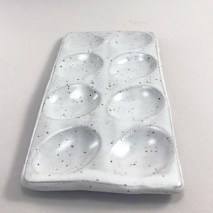 Puede incluir: Huevera de cer&aacute;mica blanca con seis hendiduras individuales. La huevera tiene un esmalte moteado.