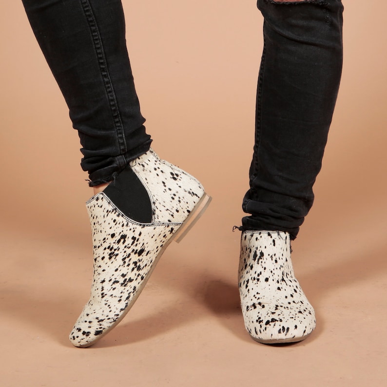 May include: White and black spotted ankle boots with a low heel and elastic side panels. The boots are paired with black denim jeans. The footwear has a unique pattern and a casual style.