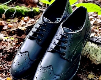 May include: A pair of black leather brogue shoes with intricate perforations and lace-up closures. The shoes are displayed on a bed of fallen leaves and wood, showcasing their classic design and craftsmanship. The shoes are a size 7.