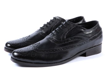 May include: A pair of black leather Oxford shoes with brogue detailing. The shoes feature a classic lace-up design and a low heel. The leather has a polished finish, and the shoes are set against a white background.