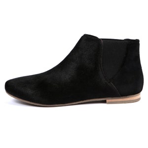 May include: Black ankle boot with a pointed toe and elastic side panel. The boot has a low heel and a textured upper. The sole is a light tan color. The boot is a slip-on style.