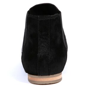 May include: Black ankle boot with a low heel. The boot features a textured, dark upper and a light-colored sole. The design includes elastic side panels for easy wear. A stylish and versatile footwear option.