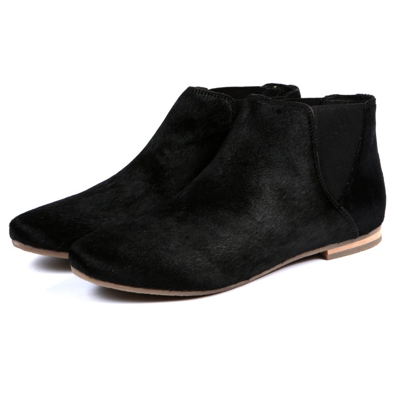 May include: A pair of black ankle boots with a low heel. The boots have a textured, fur-like appearance and a rounded toe. The sides of the boots have elastic panels for easy wear.