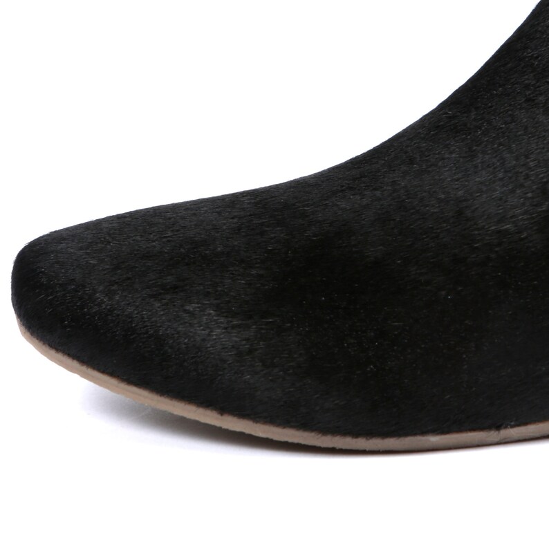 May include: Close-up of a black boot with a textured, fur-like appearance. The boot has a rounded toe and a light brown sole. The focus is on the front portion of the shoe.