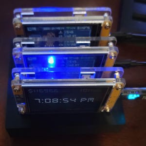 K&ouml;nnte beinhalten: Ein Stapel von vier kleinen elektronischen Ger&auml;ten mit transparenten Acrylgeh&auml;usen und blauen Lichtern. Jedes Ger&auml;t zeigt Daten auf einem kleinen Bildschirm an, wobei der untere Bildschirm "$116966" und "7:08:54 PM" anzeigt.