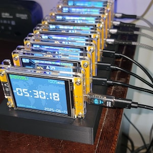 K&ouml;nnte beinhalten: Eine Reihe kleiner elektronischer Ger&auml;te mit Bildschirmen, die Daten und Uhrzeit anzeigen, verbunden durch schwarze Kabel. Die Ger&auml;te sind auf einer schwarzen Basis montiert und haben gelbe und transparente Kunststoffgeh&auml;use. Die Bildschirme zeigen die Zeit 05:30:18 an.