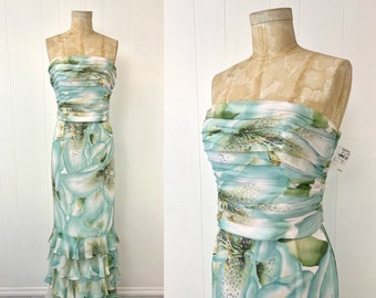 May include: A strapless maxi dress with a white background and a large blue floral print. The dress has a ruffled hem and a fitted bodice.