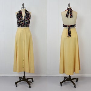 May include: A yellow maxi skirt with a button closure down the front and a black halter top with a floral print. The top is tied at the neck and back.
