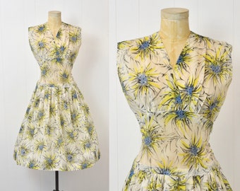 Könnte beinhalten: Ein vintage ärmelloses Kleid mit V-Ausschnitt und ausgestelltem Rock. Das Kleid hat einen cremefarbenen Hintergrund mit einem sich wiederholenden Blumenmuster in Gelb, Blau und Schwarz. Das Kleid wird auf einer Vintage-Schneiderpuppe präsentiert.
