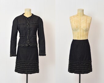 May include: A black denim skirt and jacket set with a ruffled hem. The skirt and jacket are both made of a dark denim fabric and have a frayed edge detail.