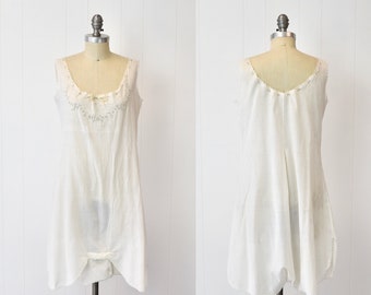 May include: A white sleeveless slip dress with a delicate lace trim around the neckline. The dress has a relaxed fit and a slightly gathered skirt.