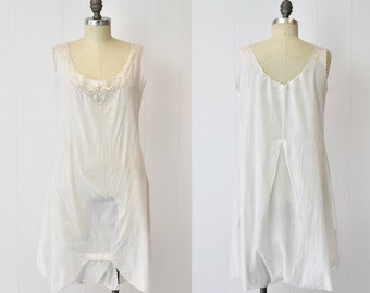 May include: A white sleeveless slip dress with a lace trim around the neckline. The dress is on a white mannequin.