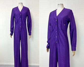 May include: A purple jumpsuit with long sleeves and a button-up front. The jumpsuit has two pockets on the chest and a V-neck.