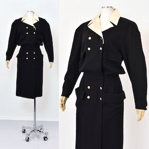 May include: A black double-breasted dress with a white collar and gold buttons. The dress has two large pockets on the front and a skirt that falls to the knees.