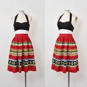 May include: A red skirt with a colorful geometric pattern. The skirt is full and has a high waist. It is made of a lightweight fabric and is perfect for summer.
